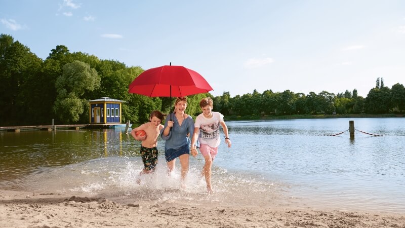 Imagebild Familie zusammen am Strand unter einem roten Schirm